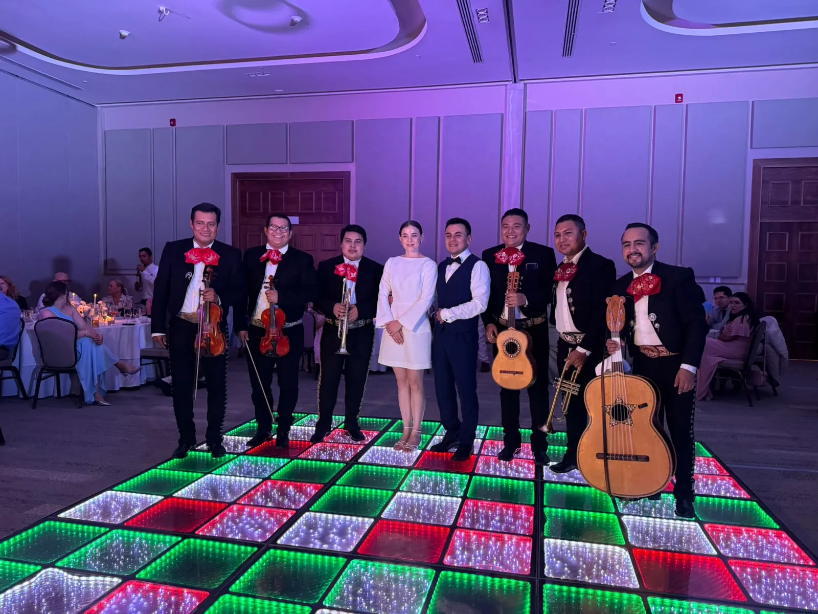 Mariachi y novios posando sobre una pista LED con los colores de la bandera de México en un salón de eventos