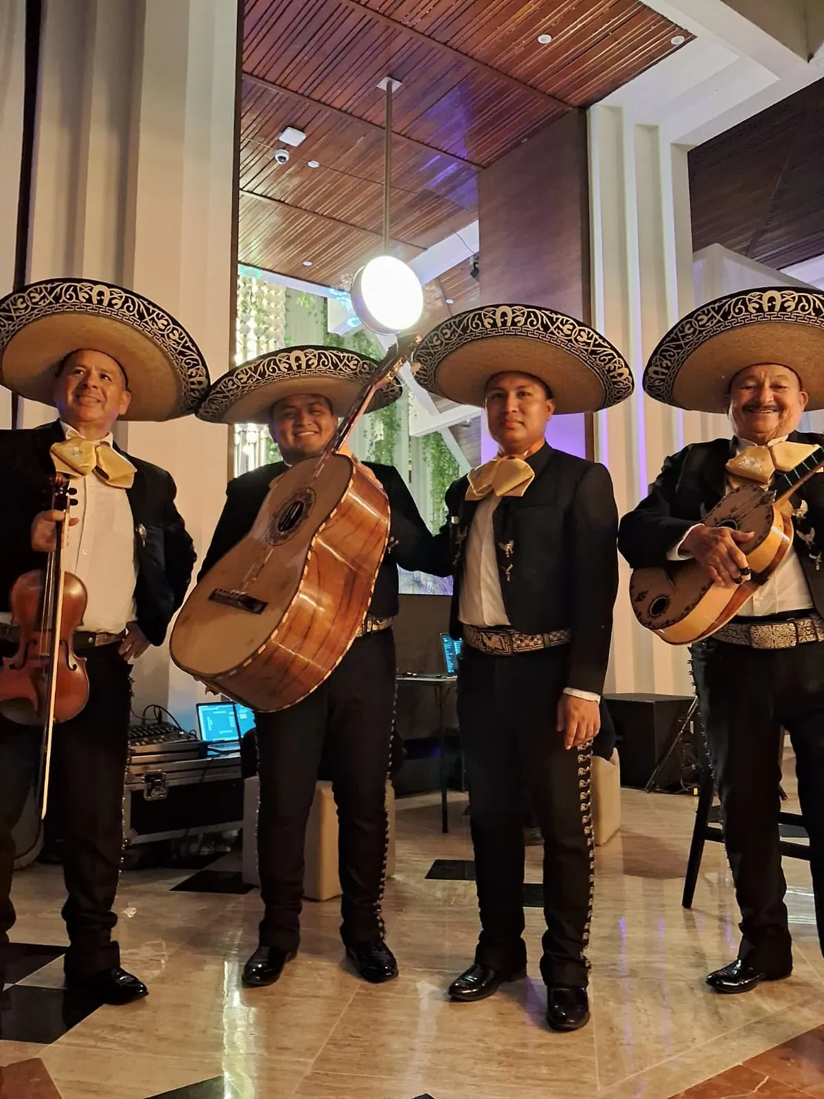 Cuatro mariachis con sombrero charro y moños dorados posando en un lobby elegante