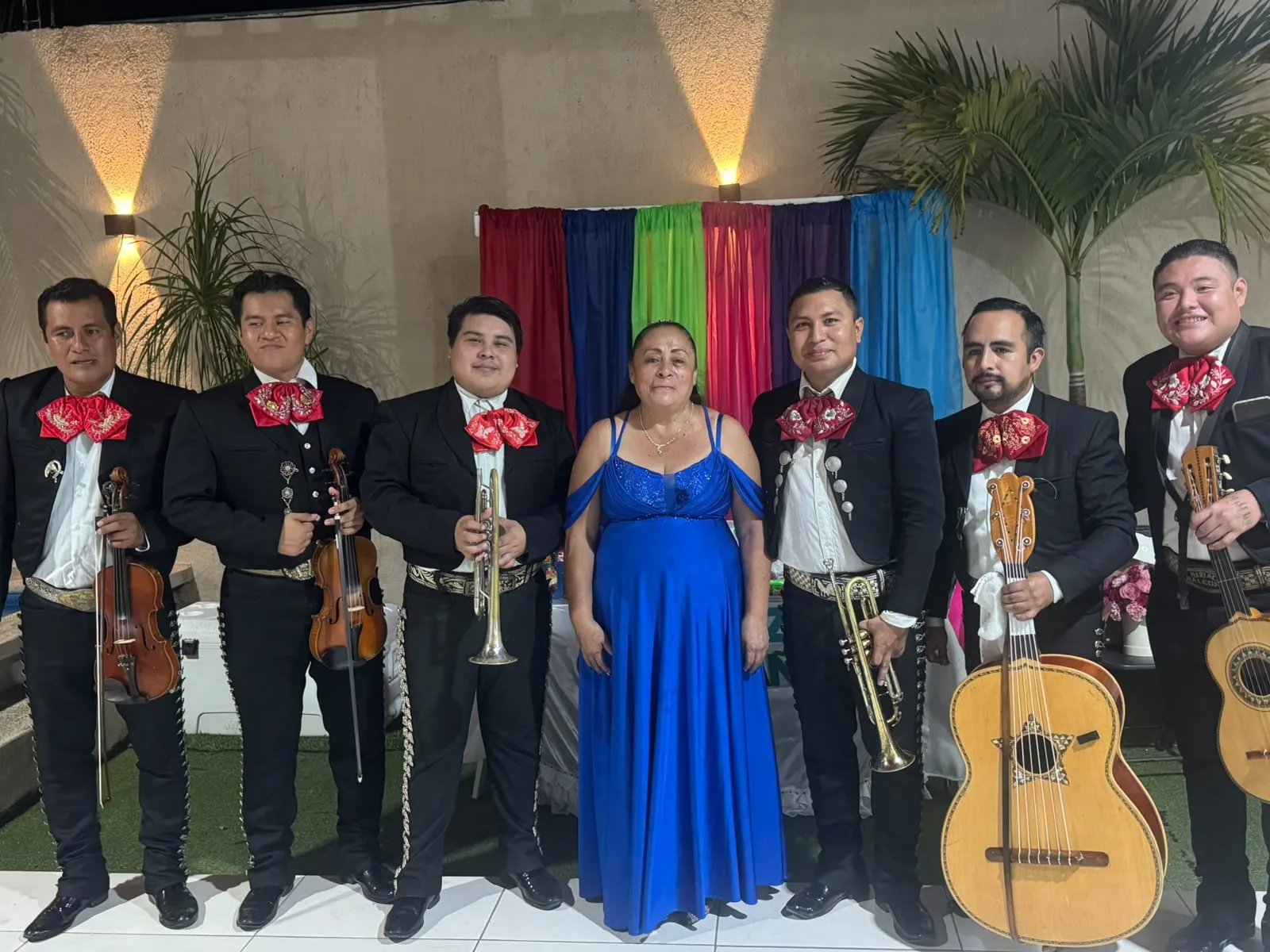 Mariachi con trompetas, violines y guitarrón dedicando una serenata de cumpleaños a una mujer con vestido azul